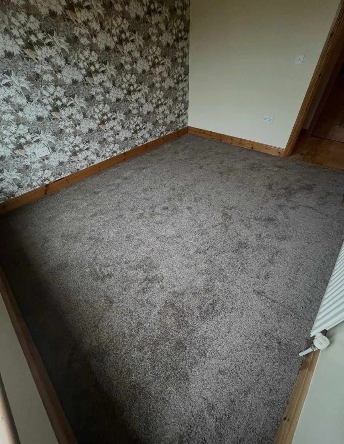 Grey carpet fitted in a room with floral wallpaper